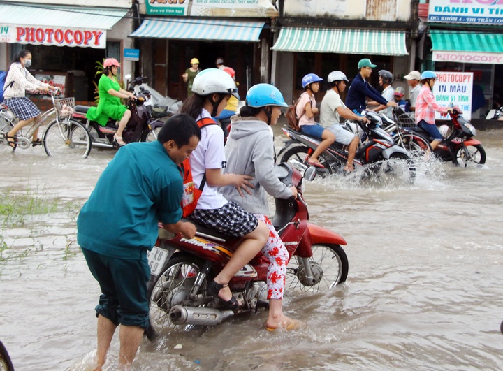 Một thanh niên đang giúp người phụ nữ chở con đi học vào sáng 18/10 qua đoạn đường ngập lênh láng ở thị trấn Long Hồ.