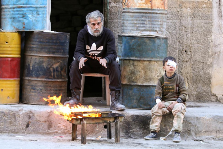 Cậu bé bị thương ở mắt ngồi cạnh một người đàn ông để sưởi ấm bên bếp củi ở khu vực do phiến quân kiểm soát ở Aleppo.