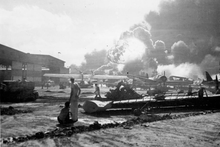 Các thủy thủ Mỹ đứng giữa các xác máy bay tại căn cứ đảo Ford. Tàu khu trục USS Shaw nổ ở giữa hậu cảnh.