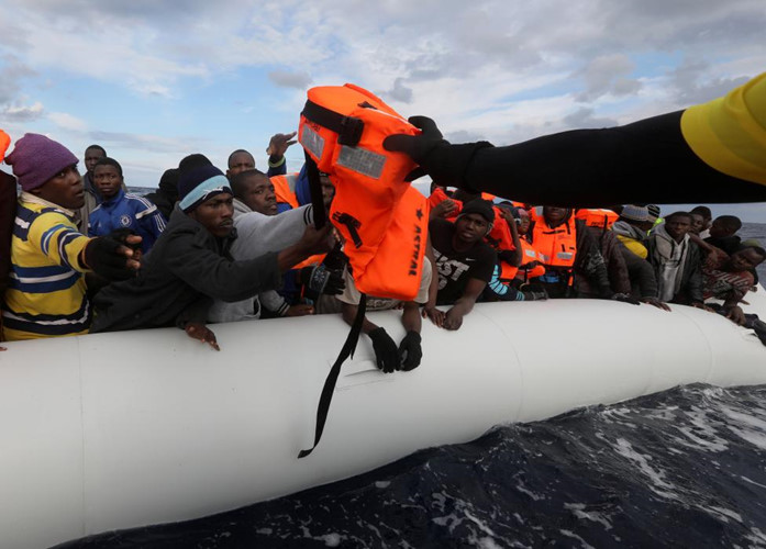 Lực lượng cứu hộ phân phát áo phao cho những người di cư trên thuyền.