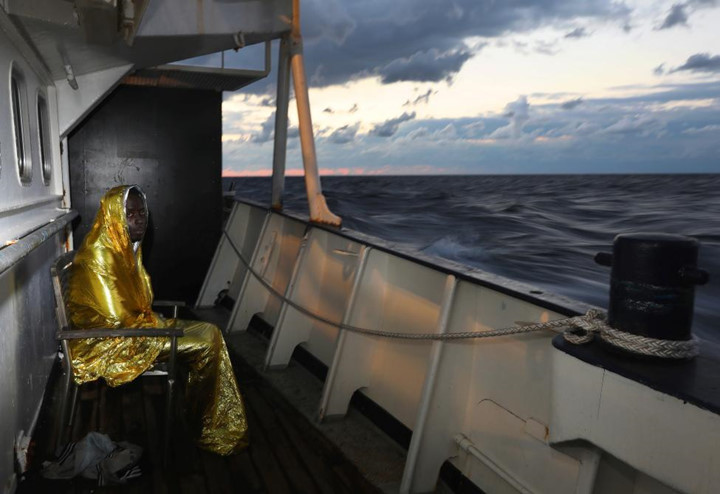 Một người di cư co ro trong chiếc chăn nhiệt ngồi ở hành lang trên boong tàu đánh cá Golfo Azzurro.