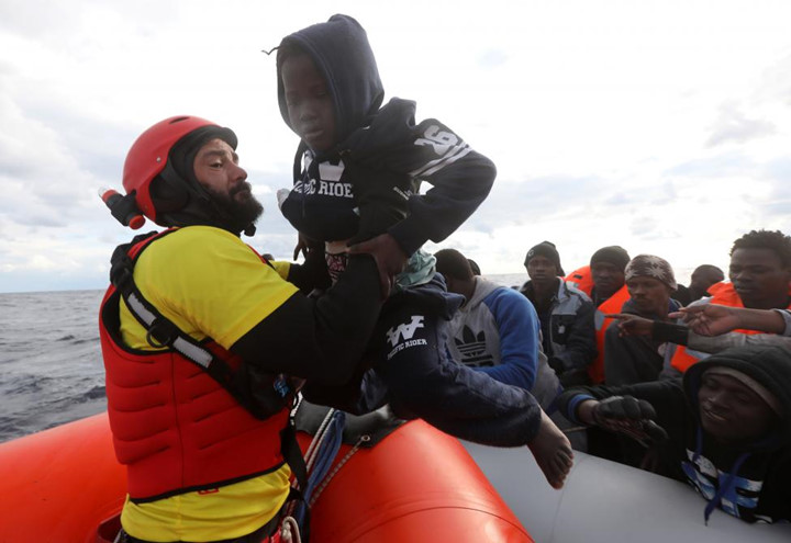 Nhân viên cứu hộ bế một đứa trẻ ra khỏi chiếc thuyền cao su chật ních người.