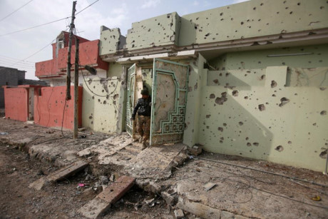 Một người lính Iraq bước ra khỏi ngôi nhà bị đạn bắn thủng lỗ chỗ sau các cuộc giao tranh với IS.