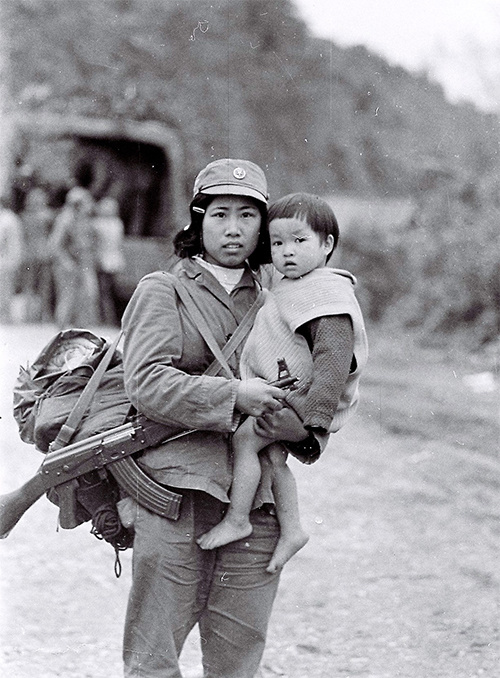 Cô bộ đội bế bé gái theo mẹ đi tản cư tại chân cầu Tài Hồ Sìn (Hòa An, Cao Bằng). Mẹ của bé trúng đạn quân Trung Quốc bị thương nặng, được bộ đội đưa về tuyến sau. 