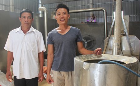 Việc đầu tư nhà máy sản xuất thức ăn viên nén giúp ông Tấn tiết kiệm chi phí thức ăn cho cá. Trong ảnh: Ông Tấn (trái) và con trai bên dây chuyền nhà máy sản xuất thức ăn viên nén.