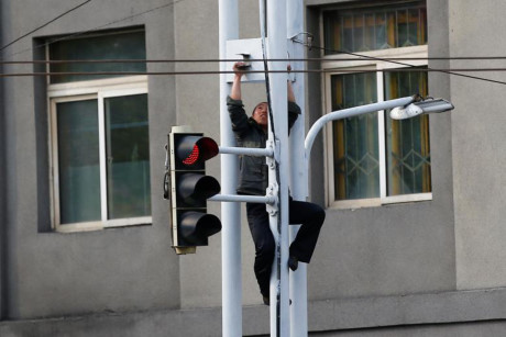 Một người đàn ông trèo lên cột đèn giao thông để sửa chữa.