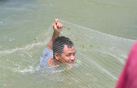 Một người dân bắt cá bằng cách dùng lưới chắn ngang dòng chảy ở phía dưới chân đập.