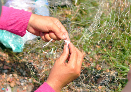 Một phụ nữ dùng dây nhựa khâu túm mắt chài bị rách để chồng đánh cá.
