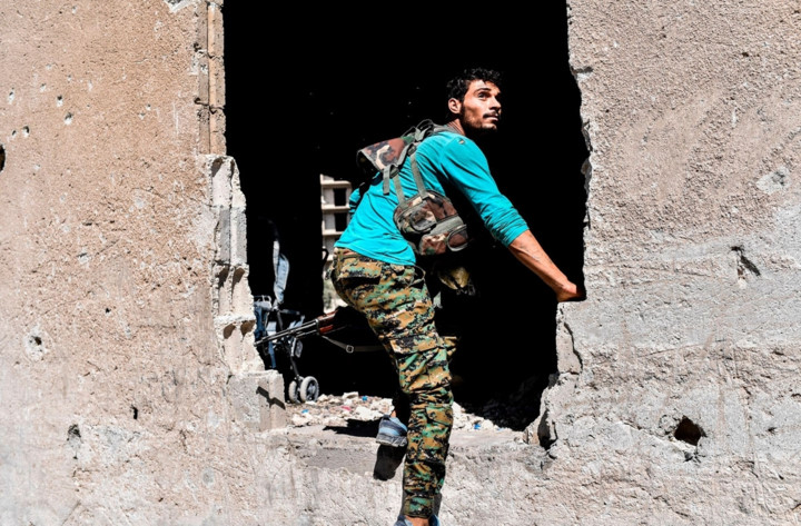 Một thành viên SDF trèo qua lỗ thủng lớn trên tường trong lúc chiến đấu với IS. Ảnh: AFP.