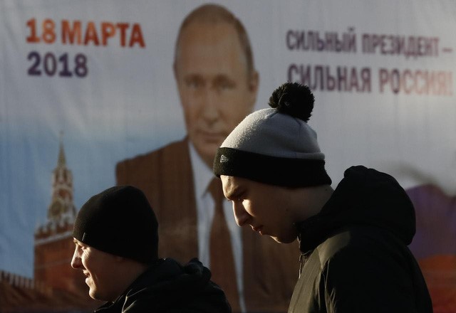 Người dân Matxcơva đi ngang bích chương vận động bầu cử của ông Putin - Ảnh: REUTERS