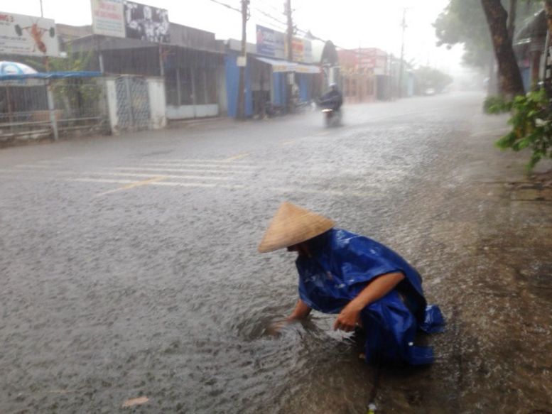 Một người dân trên đường Mậu Thân đội mưa cố móc rác chặn cống cho nước thoát nhanh hơn