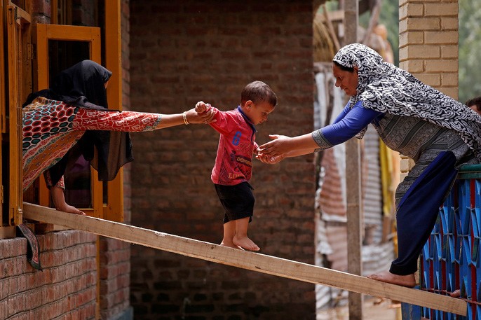 Hai người phụ nữ giúp bé trai băng qua nhà khác sau trận lũ quét ở Tailbal, ngoại ô Srinagar hôm 24/7. Ảnh: REUTERS