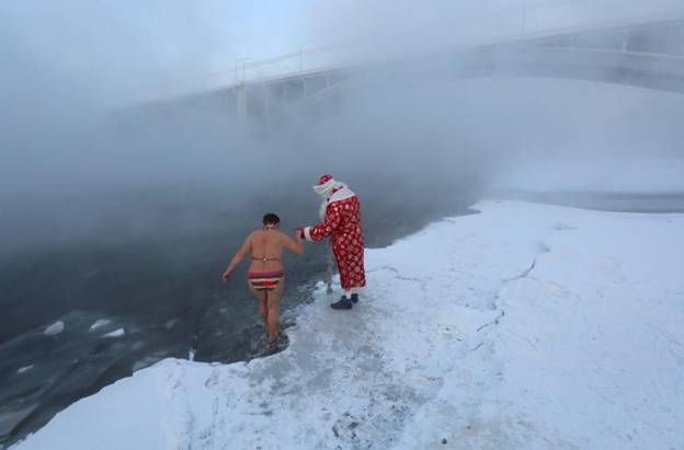 Một người đàn ông hóa trang thành Ded Moroz (ông già Noel của Nga) để giúp một thành viên của câu lạc bộ bơi lội mùa đông nghiệp dư Cryophile, đi bộ vào vùng nước băng giá của sông Yenisei để đánh dấu năm mới và mùa Giáng sinh. Nhiệt độ ngoài trời khoảng âm 26 độ C, ở Krasnoyarsk, Nga.