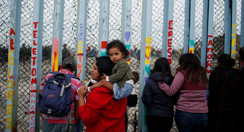 Người nhập cư đứng bên hàng rào biên giới Mỹ-Mexico. Ảnh: Reuters
