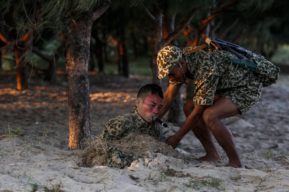 Ẩn mình dưới cát liên tục hàng giờ đồng hồ là một trong những kỹ năng được các chiến sĩ đặc công nước đặc biệt chú trọng luyện tập. Trong ảnh, một chiến sĩ đặc công nước được đồng đội hỗ trợ sau khi thực hiện nội dung ngụy trang dưới cát.