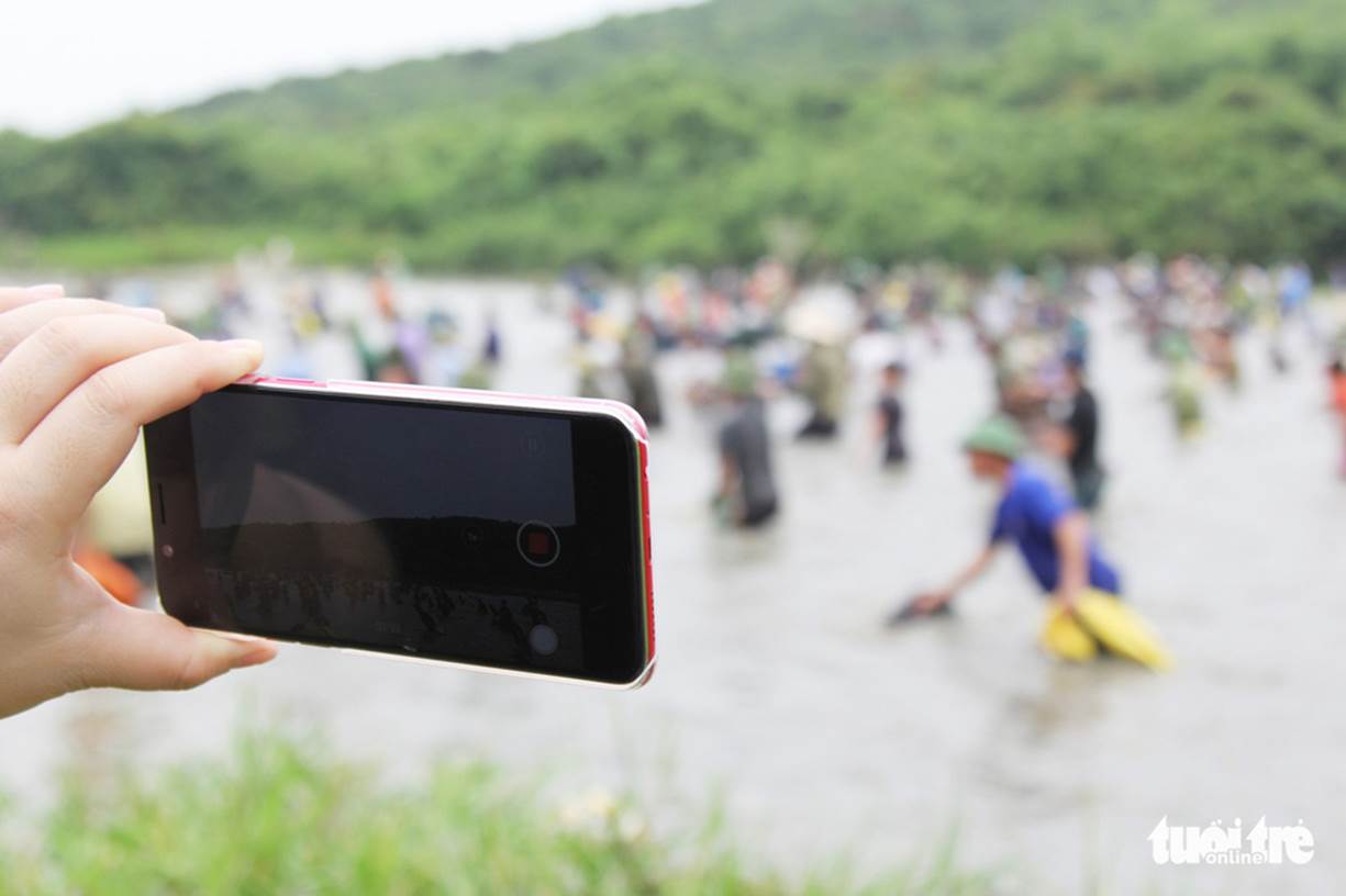 Một du khách dùng smartphone ghi lại cảnh đánh bắt cá mỗi năm mới có một lần ở lễ hội đánh cá Đồng Hoa - Ảnh: DOÃN HÒA
