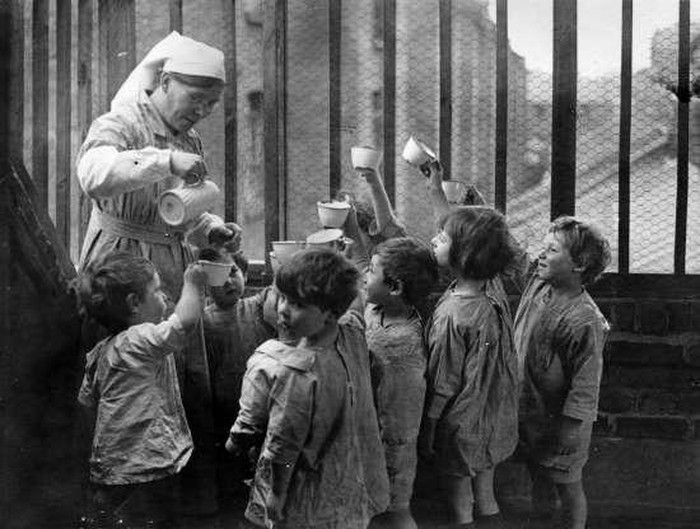 Một nữ y tá rót sữa cho những đứa trẻ tại một nhà trẻ ở Whitechapel, Anh. Cha của những đứa trẻ này đã tham gia chiến đấu cho quân Đồng minh và hy sinh.