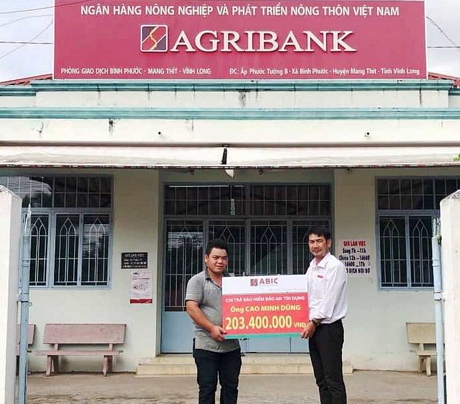 Ông Trần Hoàng Nam- Giám đốc Agribank Phòng Giao dịch Bình Phước (bên phải) trao biểu trưng chi trả bảo hiểm cho gia đình khách hàng. 