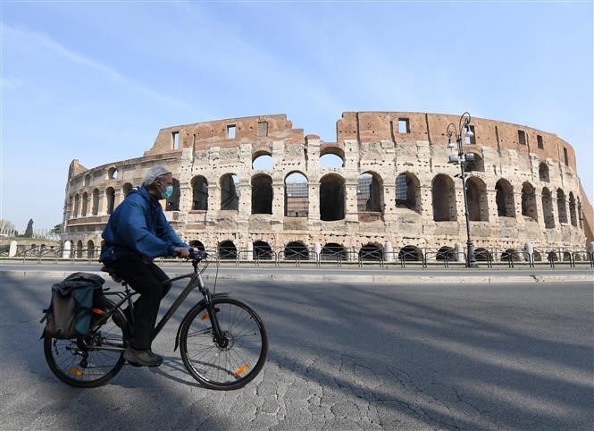 Người Italy đeo khẩu trang đạp xe qua đường phố vắng vẻ tại Rome, Italy ngày 22/3 khi dịch COVID-19 hoành hành. Ảnh: THX/TTXVN