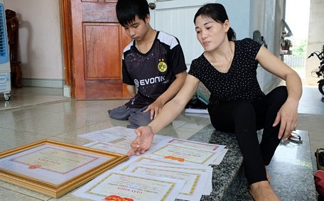  Minh và mẹ bên các tấm giấy khen, bằng khen mà Minh đạt được trong suốt quá trình học tập