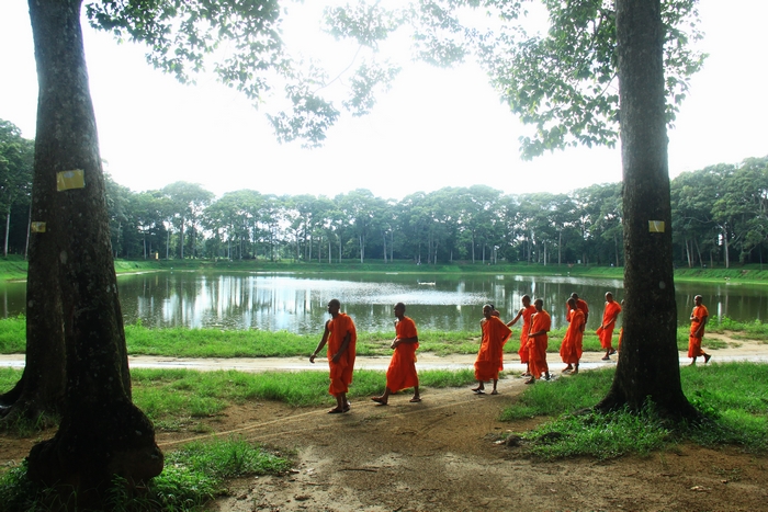Sau giờ học, từng nhóm chú tiểu của ngôi chùa Âng cạnh Ao Bà Om, đã đi vòng quanh ao Vuông, sắc áo của họ in trên mặt ao, nổi bật trên nền cây xanh ngát.