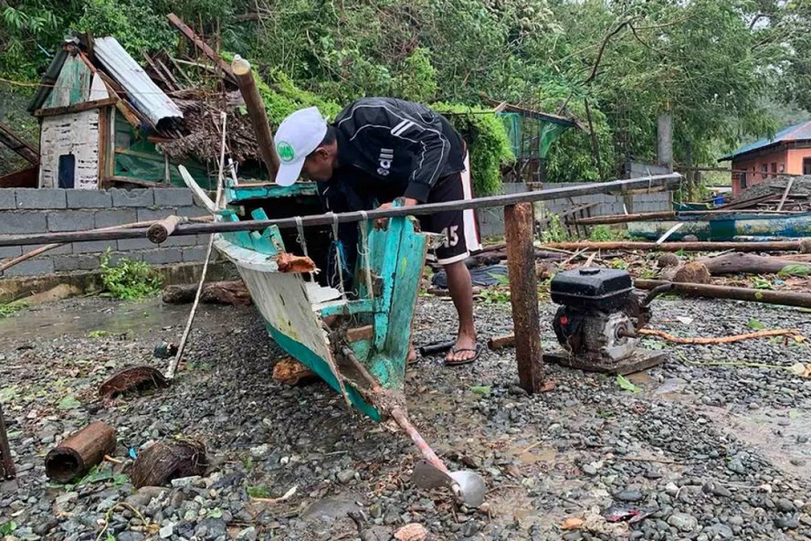 Một ngư dân kiểm tra và dọn dẹp chiếc thuyền gỗ bị phá hủy sau cơn bão. Ảnh: AFP