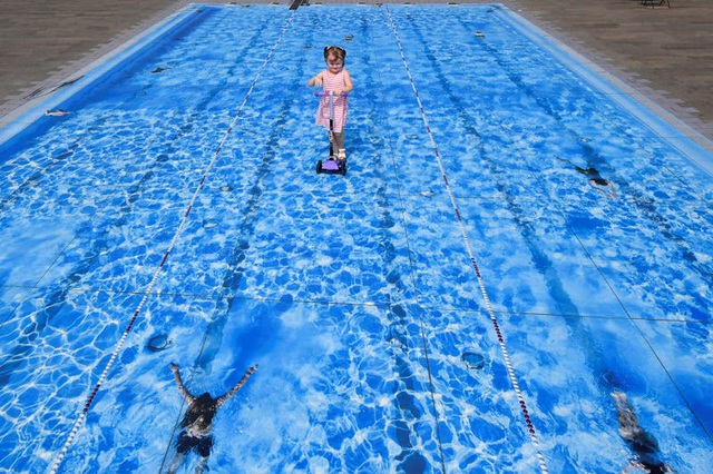 Bức ảnh này như thể chụp lại một em bé đang chạy xe trên mặt nước bể bơi, nhưng thực tế, đây là một tác phẩm được thực hiện trên nền gạch. Tác phẩm này được thực hiện tại London, Anh.