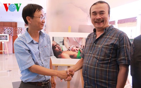Tác giả Huỳnh Nam Đông (trái) bên cạnh tác phẩm đạt giải nhất trong cuộc thi bắt tay ông Hồ Sỹ Trung, người có câu chuyện giống như nhân vật trong bức ảnh. 
