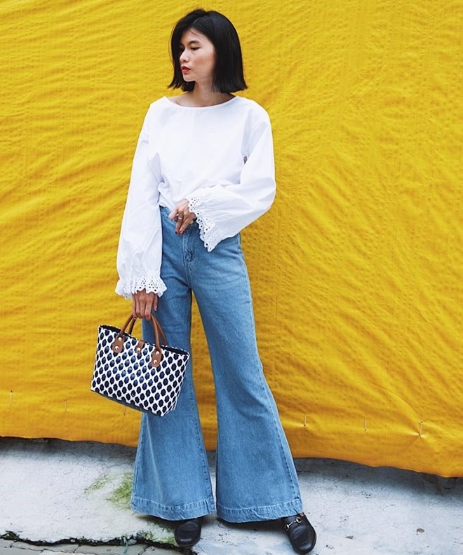 Vee Nguyễn cũng là fan của quần ống rộng với lựa chọn thiết kế denim. Cô nàng mix mẫu quần mang dấu ấn cổ điển cùng áo blouse trắng, kết hợp giày xỏ và điểm xuyết nét retro nhờ chiếc giỏ đan xinh xắn.