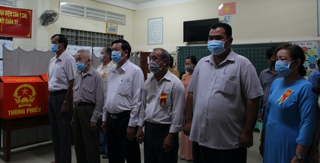 Ông Hồ Văn Huân (hàng trên, thứ 3, bên trái) cùng các cử tri và thành viên tổ bầu cử chào cờ khai mạc.