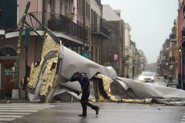 Một người đang ông đi ngang qua một phần mái nhà bị thổi bay xuống đường phố tại thành phố New Orleans, bang Louisiana. Ảnh: AP.