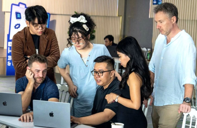 Võ Ngọc Minh Anh (hàng đứng, thứ hai từ trái qua) trao đổi ý kiến cùng mentor về sản phẩm AI Agent trong cuộc thi AI hackathon - Ảnh: NVCC