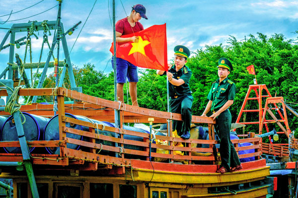 Bộ đội biên phòng hỗ trợ ngư dân treo cờ Tổ quốc kết hợp tuyên truyền phòng chống khai thác IUU trên tàu chuẩn bị ra khơi đánh bắt hải sản. Ảnh: TRUNG HIẾU

