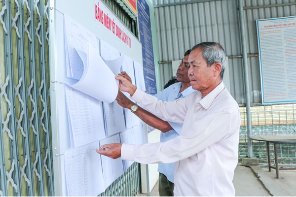 Cử tri ấp Giồng Trôm theo dõi, kiểm tra danh sách cử tri được niêm yết công khai tại Nhà văn hóa ấp.

