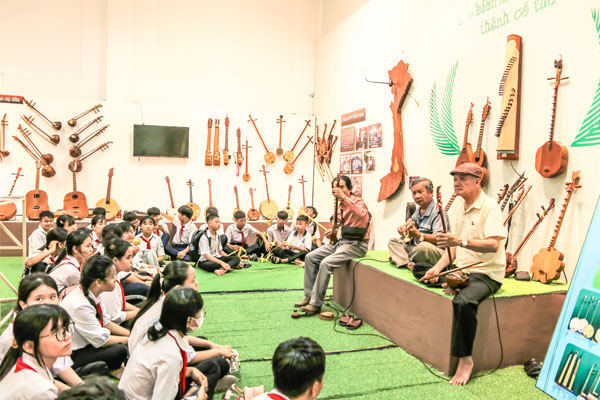 Học sinh chăm chú theo dõi Nghệ nhân dân gian Võ Văn Bá đánh đờn cò từ gỗ dừa trong “Giờ học di sản”.

