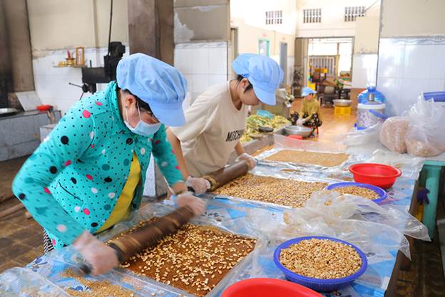 Đậu phộng béo giòn được những người thợ nhanh tay cán hòa lẫn vào mẻ kẹo khóm lúc còn nóng