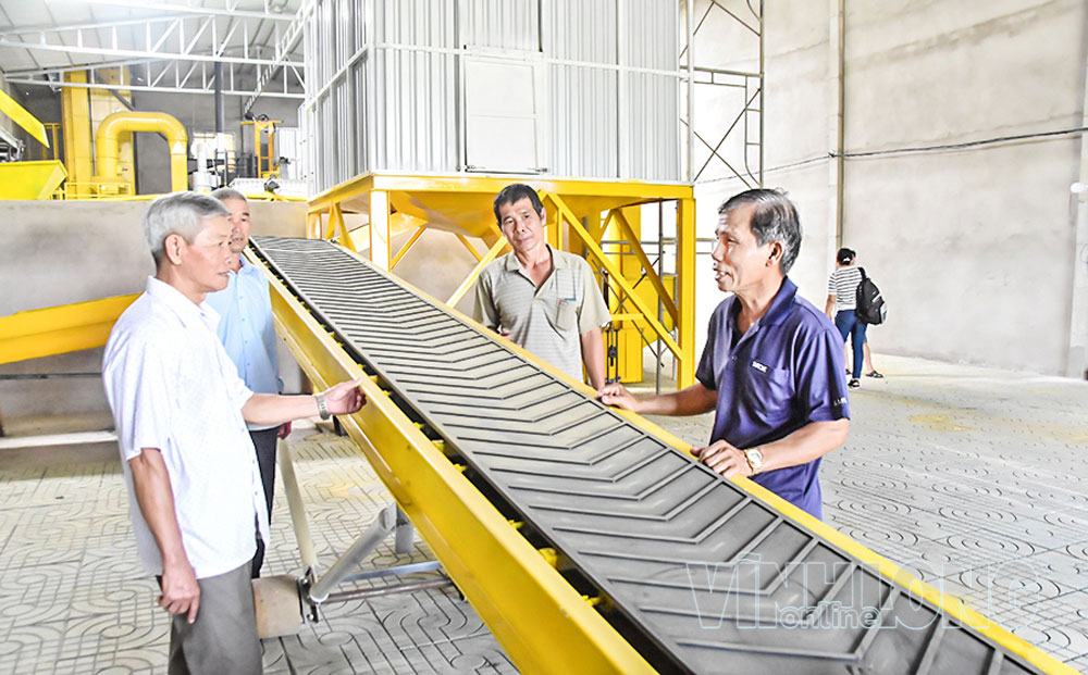 Giám đốc HTX Nông nghiệp Phát Tài Trần Văn Chung (bên phải) chia sẻ quy trình vận hành dây chuyền sản xuất lúa giống và hệ thống sấy lúa của HTX. Ảnh: MỸ NHÂN

