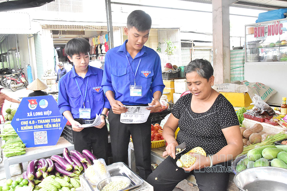 Đoàn viên, thanh niên tuyên truyền, vận động tiểu thương tham gia thanh toán không dùng tiền mặt tại chợ Long Hiệp. Ảnh: MỸ NHÂN

