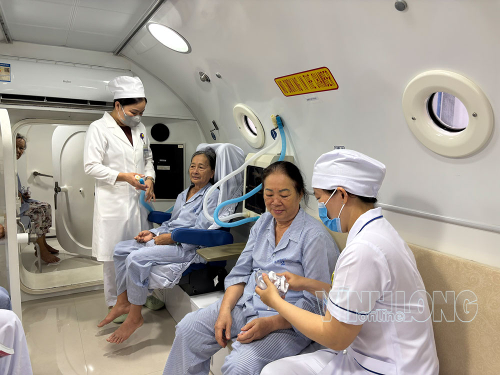 Cán bộ y tế Bệnh viện Y học cổ truyền Trần Văn An hỗ trợ bệnh nhân chạy hệ thống oxy cao áp. Ảnh: PHAN HÂN


