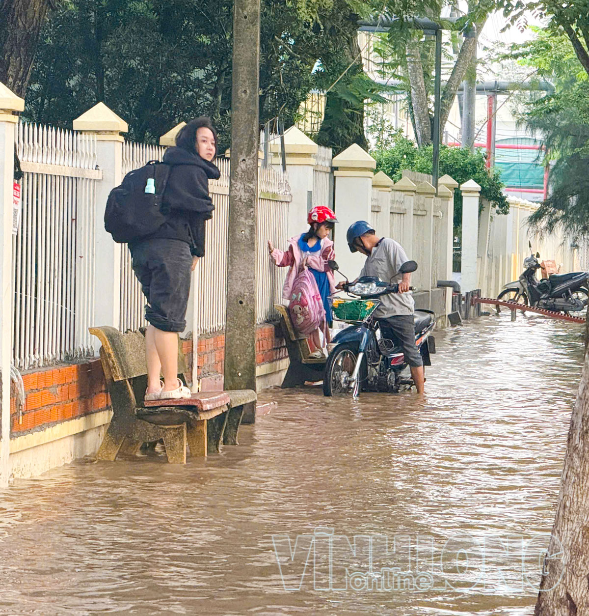 Phụ huynh và học sinh di chuyển chậm qua đoạn đường ngập sâu trong giờ cao điểm.

