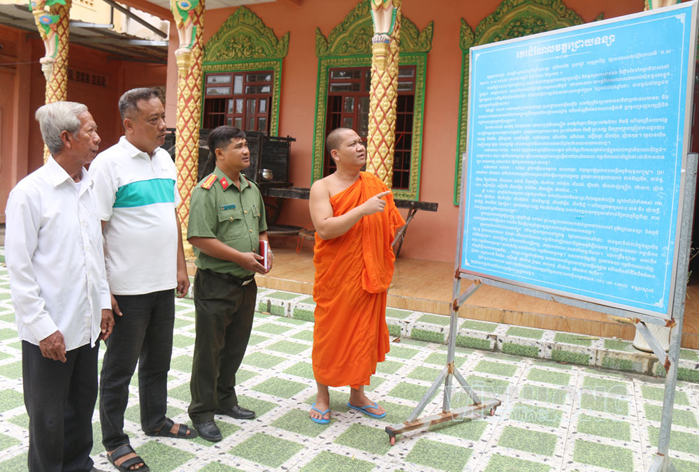 Đại đức Giang Sô Thanh giới thiệu những dấu mốc lịch sử, cách mạng của chùa Chrôi Tansa qua bảng tư liệu với cán bộ Công an và người dân địa phương. Ảnh Su Chịa.
