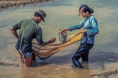 Hai vợ chồng đang mò cua bắt ốc bên một cái ao.