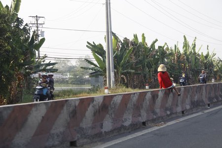 Người đi bộ trèo qua dải phân cách trên QL1 để sang đường. Đây là hành vi vô cùng nguy hiểm cho bản thân, bởi trên QL1 lưu lượng xe nhiều, xe tải trọng lớn và vận tốc cao.