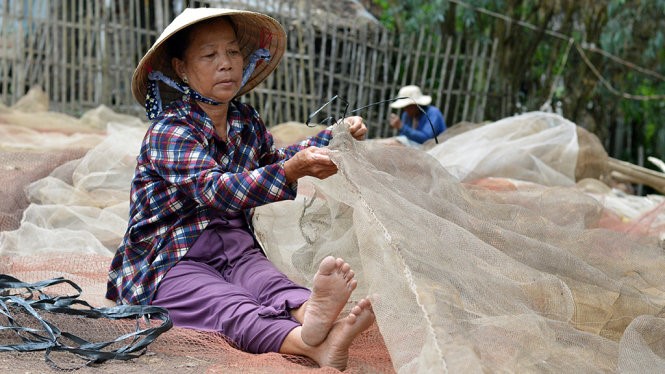 Bà Sương có thâm niên 10 năm trong nghề câu lưới tranh thủ vá lưới để kịp con nước về - Ảnh: NGỌC TÀI