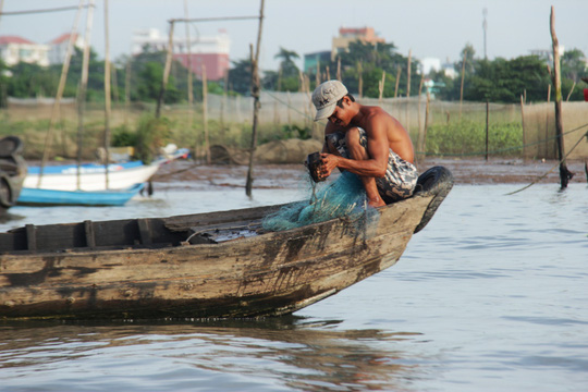 Một người đàn ông đang ngồi gỡ lưới cá, chuẩn bị cho một ngày mới