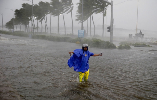 Philippines đã huy động đông đảo các binh sĩ, cảnh sát và các đội cứu hộ để giúp người dân sơ tán và khắc phục hậu quả do bão Mangkhut gây ra. Trong ảnh: Cảnh sát giao thông hướng dẫn các phương tiện di chuyển trên đường ngập nước ở thủ đô Manila, Philippines. (Ảnh: Bloomberg)