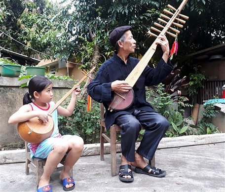 Nghệ nhân Dương Văn Thục truyền dạy cách đàn tính, hát then cho người cháu của mình. (Ảnh: Đức Hiếu/TTXVN)