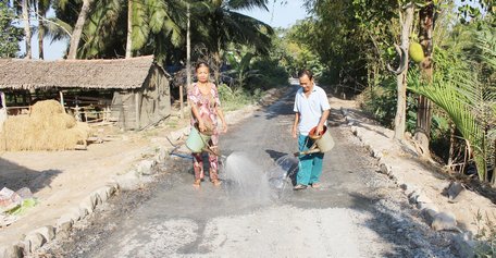 Vợ chồng ông Me tưới nước cho đỡ bụi trong khi chờ tuyến đường hoàn thành.