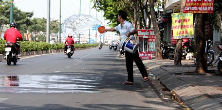  Một nhân viên quán cà phê trên đường Phạm Văn Đồng, TP.HCM tưới nước xuống mặt đường để giảm nhiệt trưa 27/3 - Ảnh: QUANG KHẢI