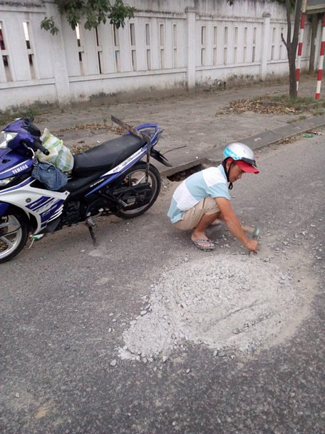 Hai thợ nề đục đẽo dẹp khối bêtông đổ giữa đường để xe không tai nạn